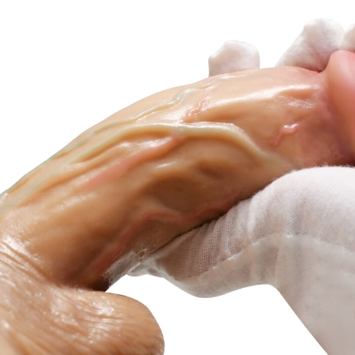 A close-up of gloved hands holding the Female Wearable Simulation Electric Retractable Dildo Masturbator (Lala Les II), detailed with intricate features, like visible veins and lifelike skin texture in natural beige and light pink hues. The background is plain white.