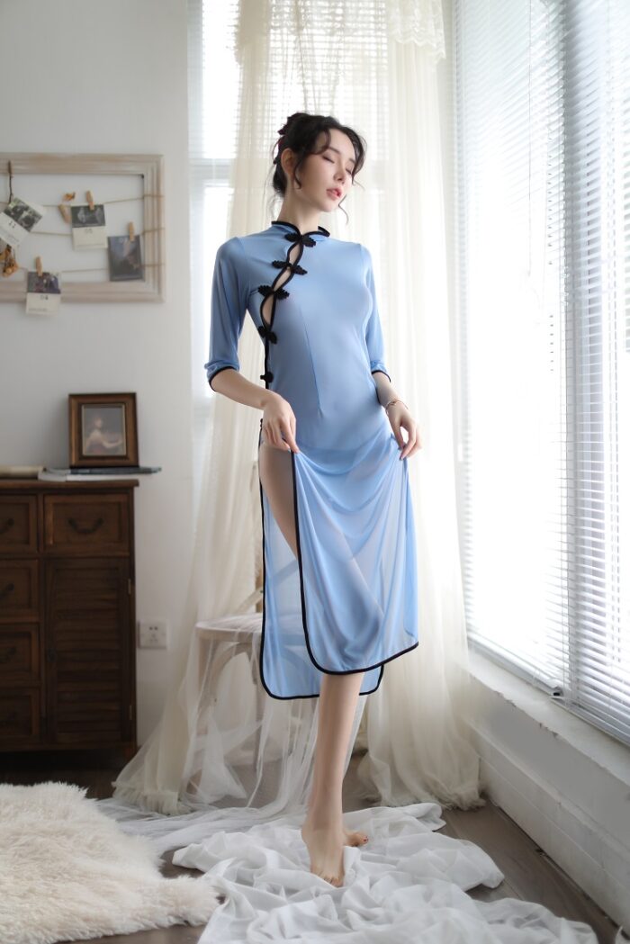 A woman with black hair wearing a light blue qipao with black trim, standing against a white background and holding a black fan with golden patterns.