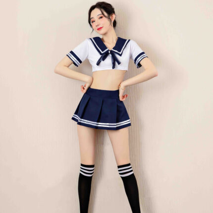 A woman is dressed in a sailor-themed outfit consisting of a short-sleeved white crop top with navy blue accents, a matching navy blue mini skirt, and knee-high black socks with white stripes. She stands confidently with her hands on her hips, showcasing the playful and youthful style of her ensemble.