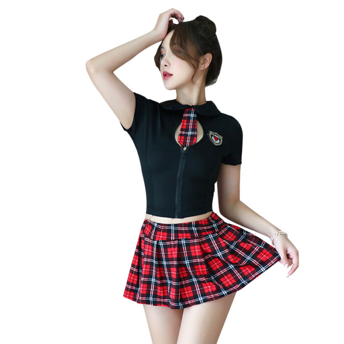 A woman is wearing a black crop top with a small cutout at the chest and a plaid tie. The top is paired with a red and black plaid mini skirt. Her hand is lifting the skirt slightly, and her other hand is touching her hair, giving a playful and stylish pose.