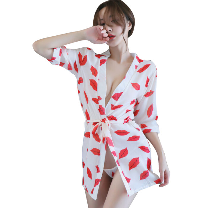 A woman is wearing a white robe adorned with a red lips print pattern. The robe is loosely tied at the waist, revealing a glimpse of her underwear. She strikes a casual pose, with one hand touching her face and the other resting by her side. The overall look is playful and flirty.