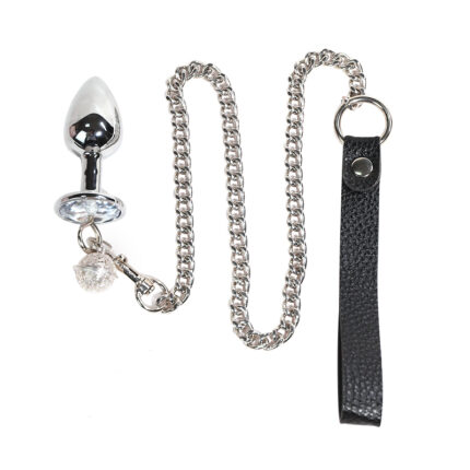 a stainless steel butt plug with an attached leash. The plug is designed with a tapered end for easy insertion and a flared base to prevent it from slipping inside. The base of the plug is adorned with a decorative gemstone, adding a touch of elegance. The leash is attached to the plug via a chain, and it includes a leather loop handle for ease of use. This type of product is typically used in BDSM and fetish play, offering a combination of anal stimulation and control dynamics between partners.