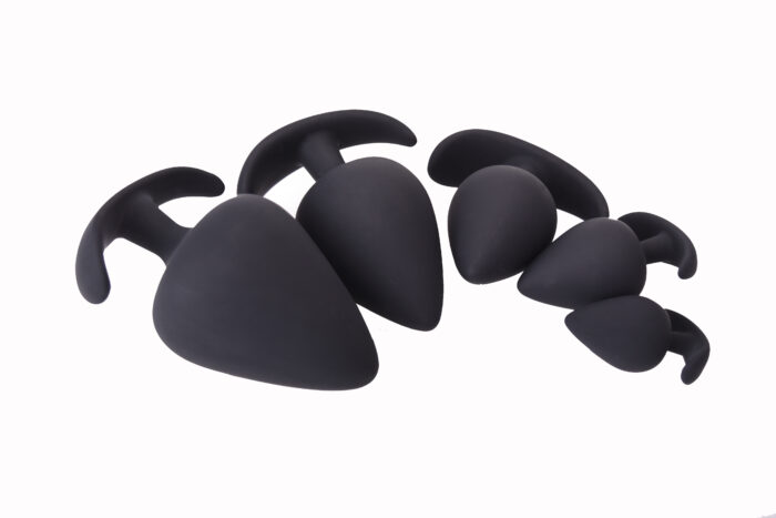 a set of black silicone anal plugs in various sizes. Each plug has a broad, triangular shape with a tapered tip for comfortable insertion and a curved, T-shaped base for easy removal and safety. The smooth texture of the silicone material ensures a pleasurable experience, making this set ideal for users at different stages of experience and comfort levels.