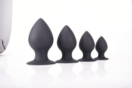 a set of four black silicone butt plugs in different sizes, arranged in a row from largest to smallest. The plugs have a bulbous, tapered design with a flared base for safety and comfort during use. The smooth texture and varying sizes make them suitable for different levels of experience, allowing for gradual progression in anal play.